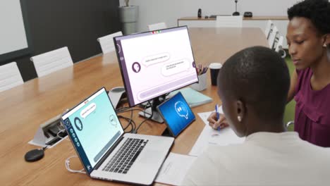 African-american-businesswomen-talking-and-using-technology-with-digital-chat-on-screens-in-office