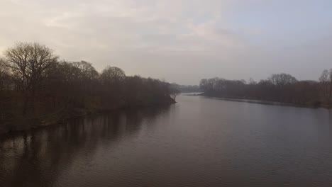 Flying-along-misty-lake-with-woodland-either-side-of-shot