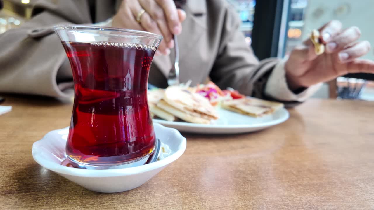 Ahşap bir masada, yemek yiyen bir kişinin olduğu Türk çayının yakın çekimi.