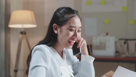 close up of asian woman designer talking on smartphone while looking at the layout bond in hand at the office