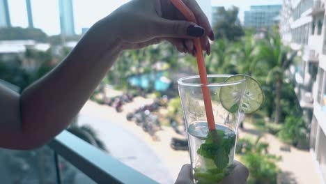 girl with long nails mixes mojito with straw on terrace