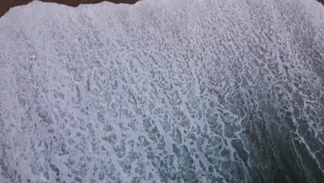 an unusual top down shot of the waves of the untamed ocean washing over a sandy beach