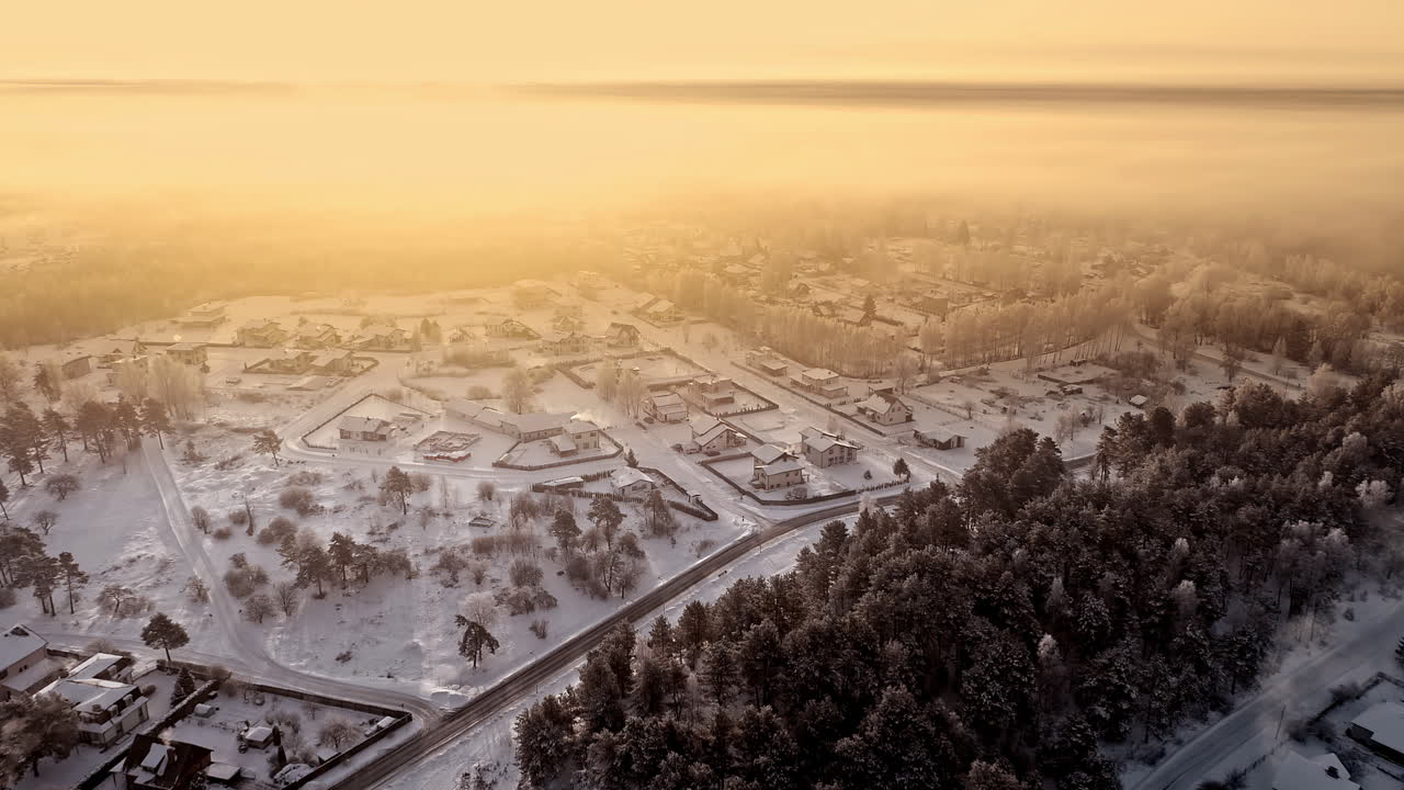 황금빛 일몰 동안 시골 지역의 눈 덮인 마을 위로 공중 비행 - 태양 광선에 눈 덮인 집들이 있는 겨울 원더랜드