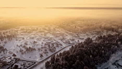 aerial flight over snowy village in rural area during golden sunset - winter wonderland with snow-covered houses lighting in sun rays