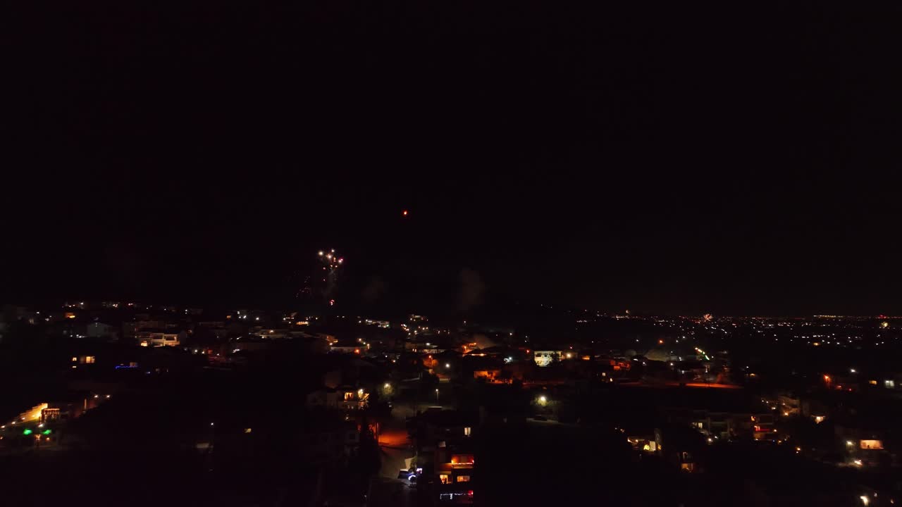 Aerial fly city illuminated at night below Christmas Eve, New Year fireworks explosions in the sky