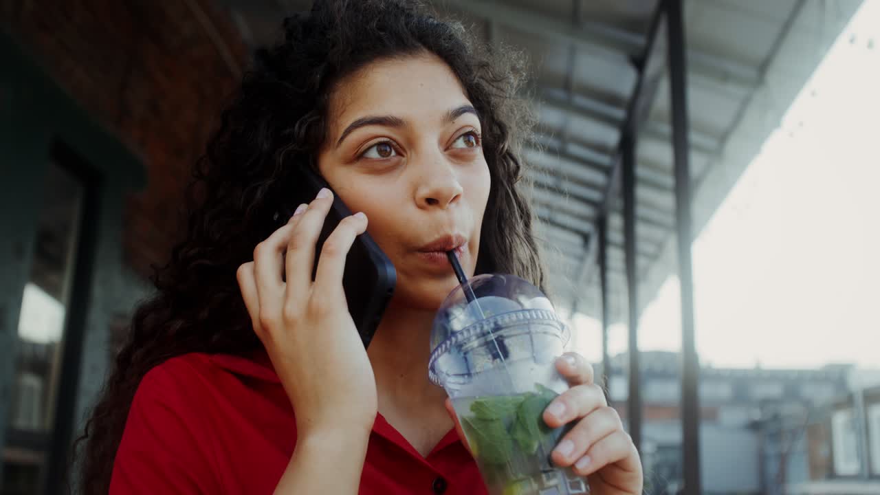 Woman talking on phone and drinking a beverage outside