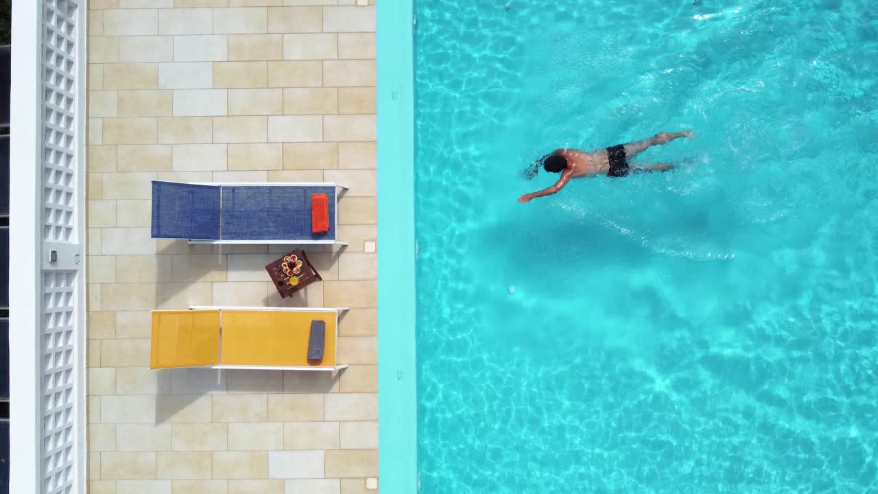 Draufsicht auf einen Mann, der aus einem Resort-Schwimmbad schwimmt, Sommerurlaub.