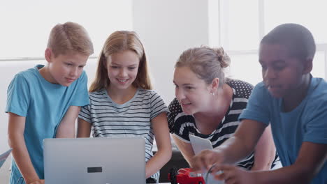 students with female teacher in after school computer coding class learning to build robot vehicle