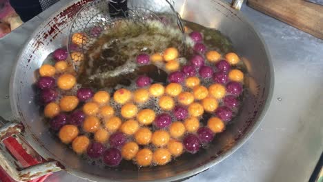 cooking quail candy eggs or turtle eggs sweets in big pan with hot oil, thai traditional dessert snack made from cassava flour (tapioca starch) and sweet potato at the market. 4k footage.