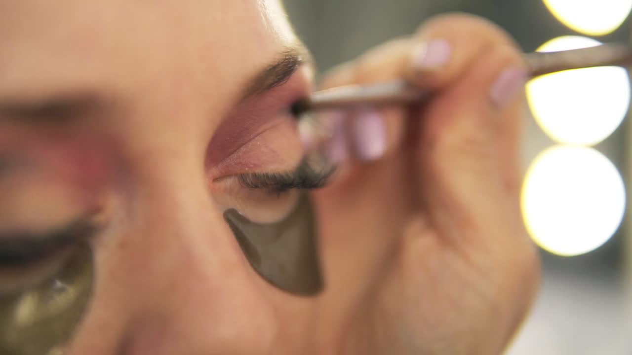Make-up artist applying eye shadow to model's eye. Close up view. Patches