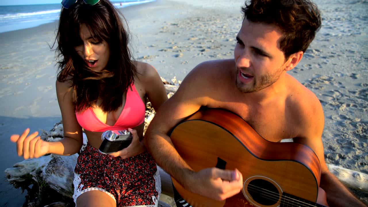 una pareja multiétnica tocando la guitarra en unas vacaciones en la playa.