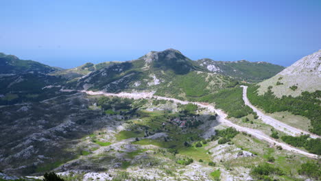 View-of-the-vast-mountainous-landscape-with-green-valley,-roads-and-rocks-from-the-Njegos-Mausoleum-atop-the-Mount-Lovcen-in-Montenegro,-Balkan,-blue-sky-above-tall-mountains,-scenic-static-4k-shot