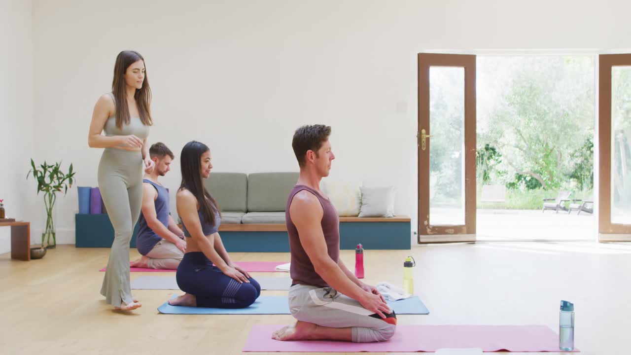 여성 강사가 도와주는 수업에서 매트에 무 ⁇ 을  ⁇ 고 요가를 연습하는 다양한 그룹