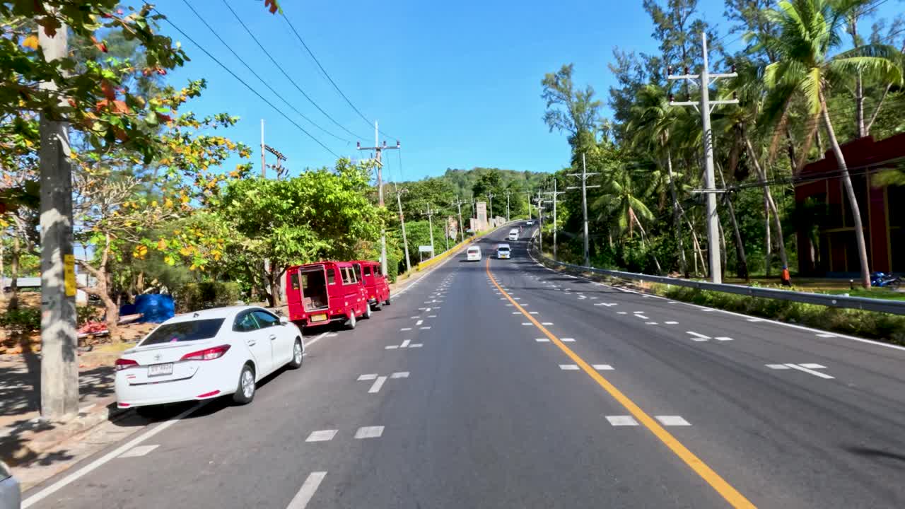 Daytime vehicle journey on tropical city street with palm trees, parked cars, and clear skies
