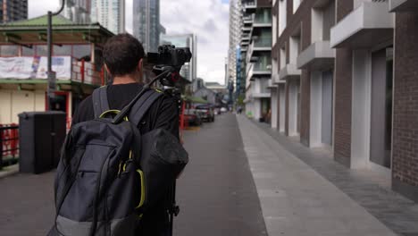 young caucasian man is walking with his backpack and camera tripod on his back in the streets of the business district canary wharf in london in autumn