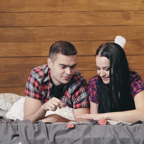 enamored couple are lying on the bed and throwing up red paper hearts with their hands on the background of wooden wall on valentine's day