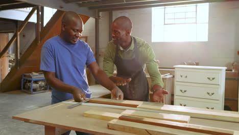 after measuring african american male colleagues marking cuts with tape, square in shop for project