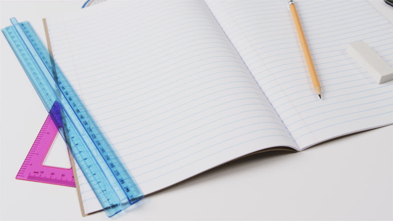 primer plano de un cuaderno abierto con papelería escolar sobre un fondo gris, en cámara lenta