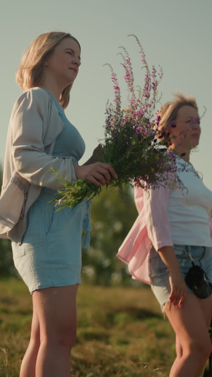 젊은 여성은 가게 미소 짓고, 보라색 꽃의 꽃줄기를 들고 멀리 을 가리키며, 밝은 빛의 날, 빛이 그녀의 얼굴에서 반사되는 바에 서서 평화로운 순간을 즐기고 있습니다.