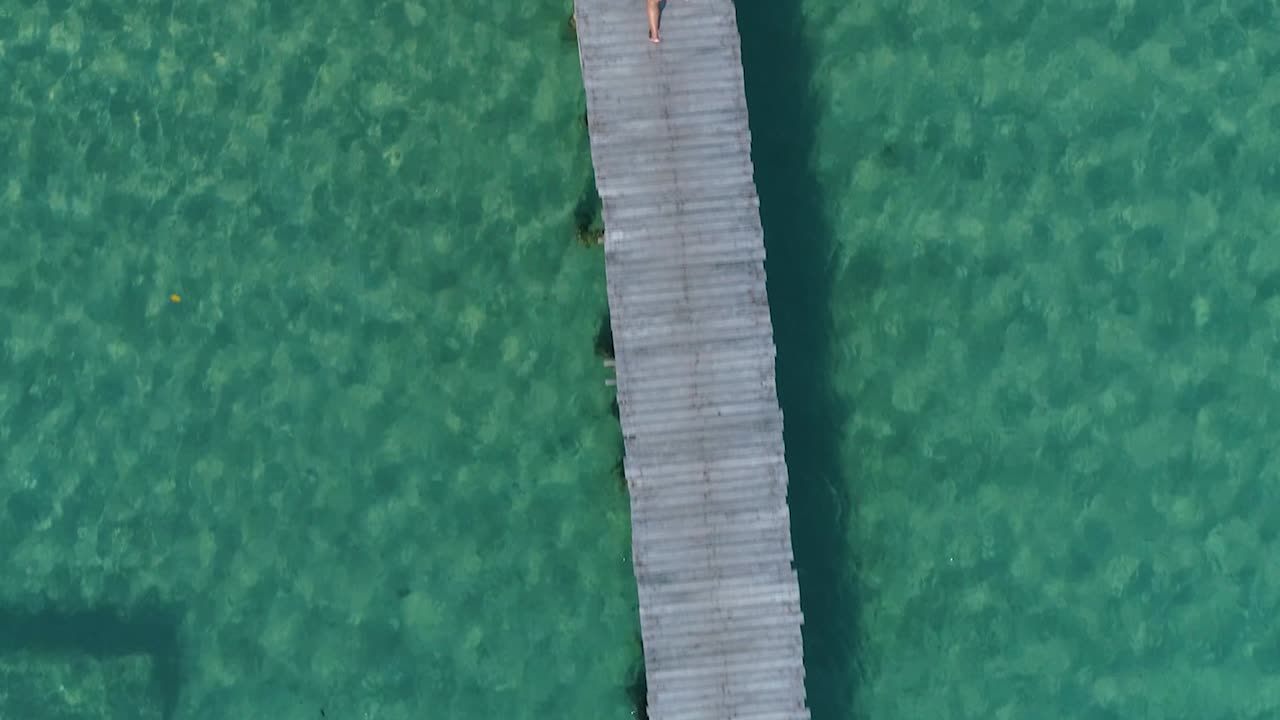 Ripresa aerea di una ragazza in bikini giallo che cammina da sola su un molo, con visuale verso il basso