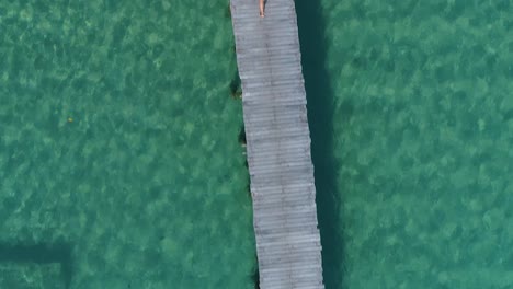 Antena-De-Una-Chica-En-Bikini-Amarillo-Caminando-Sola-En-Un-Muelle,-Con-La-Cámara-Hacia-Abajo