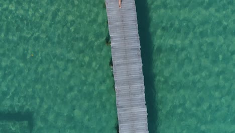 antena de una chica en bikini amarillo caminando sola en un muelle, con la cámara hacia abajo