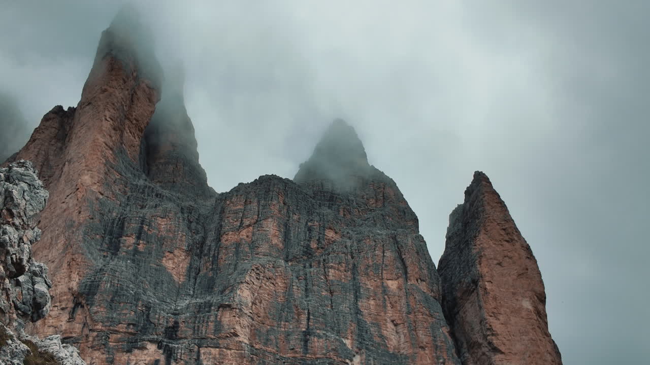 Drifting clouds swirling around dramatic rocky peaks of Tre Cime di Lavaredo rising through misty Dolomites mountain landscape in Italian Alps