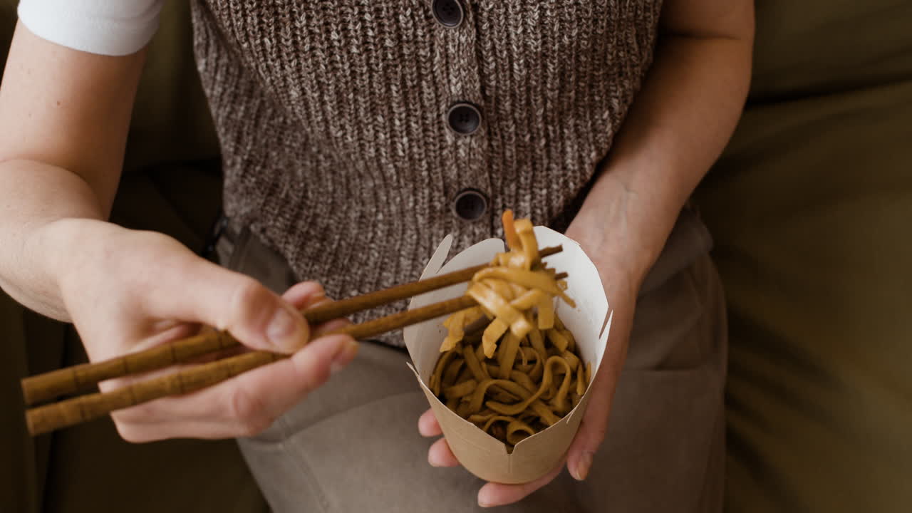 Person eating noodles with chopsticks from a take-out container