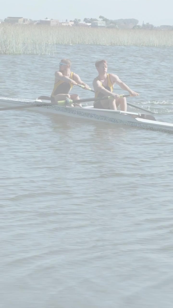 Vertikal video: To mandlige atleter ror ved start, driver dobbeltsculler for at flytte båd forbi siv