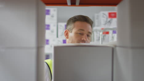 Female-Worker-Wearing-Headset-In-Logistics-Distribution-Warehouse-Taking-Box-Off-Shelf