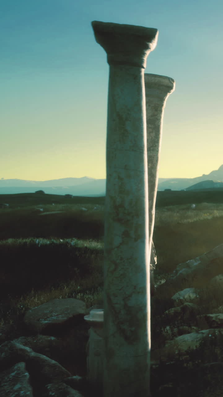 Antiche colonne si ergono solitarie in un campo aperto al tramonto in una zona rurale.
