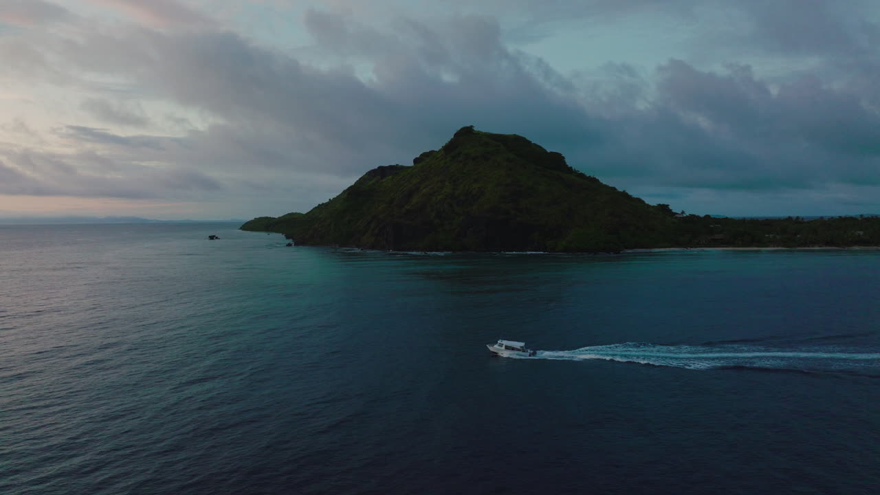 Tour boat navigates tranquil waters past island at golden hour in stunning aerial