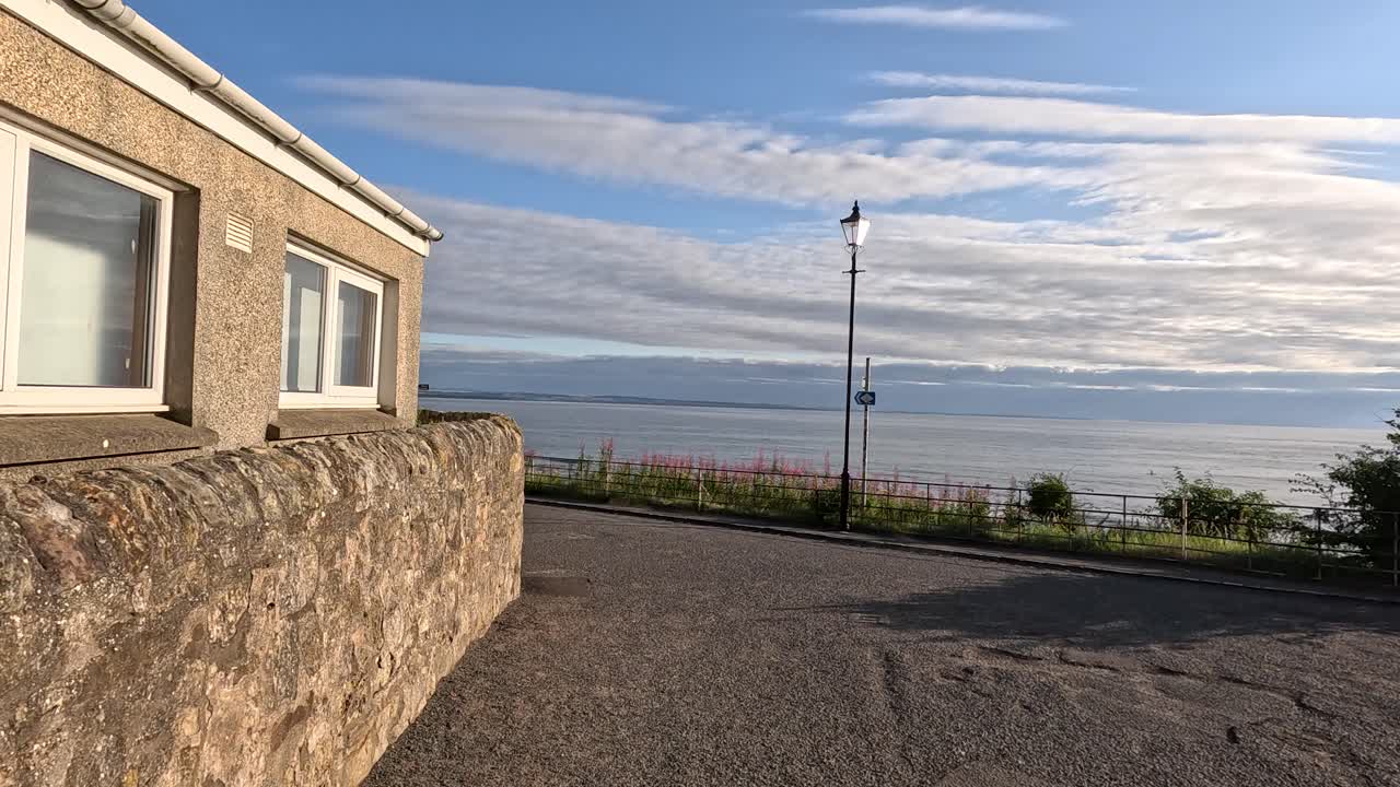Camera moves through stone alleyway, revealing seaside village, ocean horizon, and tranquil evening light