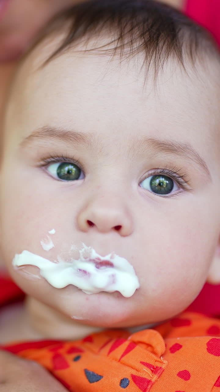 Beautiful baby murky from food he is being fed with. Mom gives a spoon to her child but he turns the head away. Close up. Vertical video