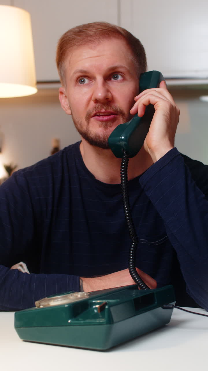 Young man answers vintage wired telephone smiles with nostalgia says hello warm call indoors evening