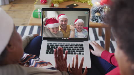 african american mother and daughter using laptop for christmas video call with family on screen