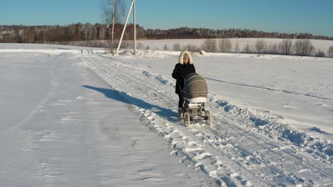 Mutter-In-Dunkler-Winterjacke-Geht-Mit-Kinderwagen-Auf-Verschneiter-Landstraße-Spazieren