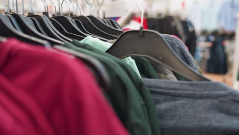 view of browsing through clothes on racks in a mall, with a hand picking one garment. captured with a handheld camera, this video highlights the shopping experience and detailed textures of clothing