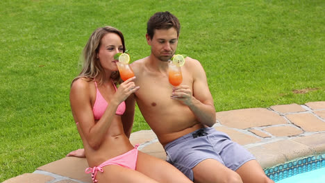 sexy couple sitting by the pool on holidays drinking cocktails