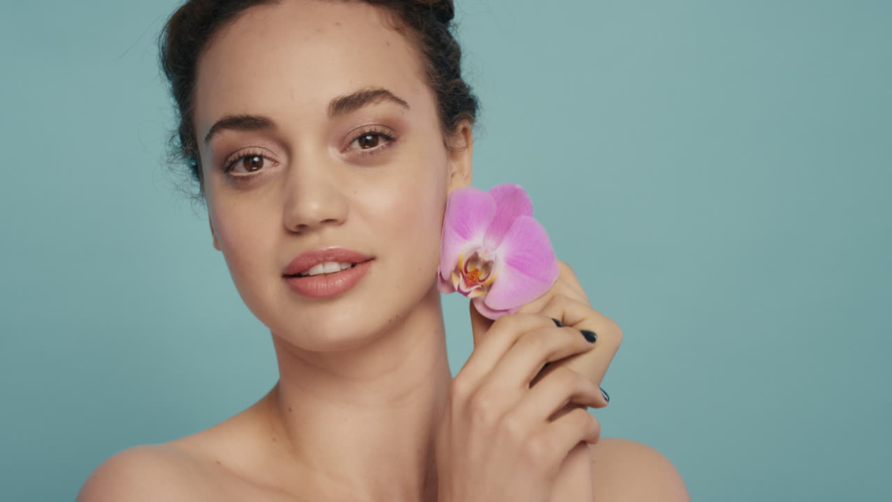 ritratto di bellezza bella donna viso toccante con colorato rosa fiore d'orchidea carezza liscia pelle sana carnagione godendo di fresca fragranza naturale concetto di cura della pelle
