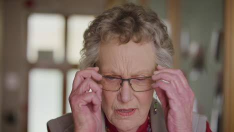 portrait of old retired woman putting on glasses in retirement home eyesight vision