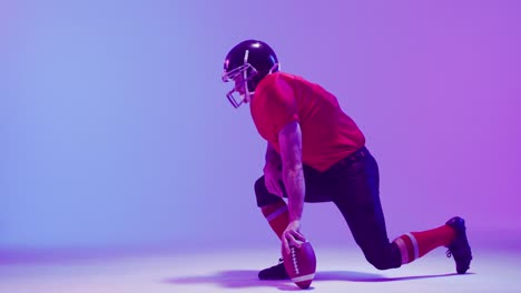 Video-Eines-Kaukasischen-American-Football-Spielers-Mit-Helm-Und-Ball,-Der-Vor-Neonviolettem-Hintergrund-Kniet