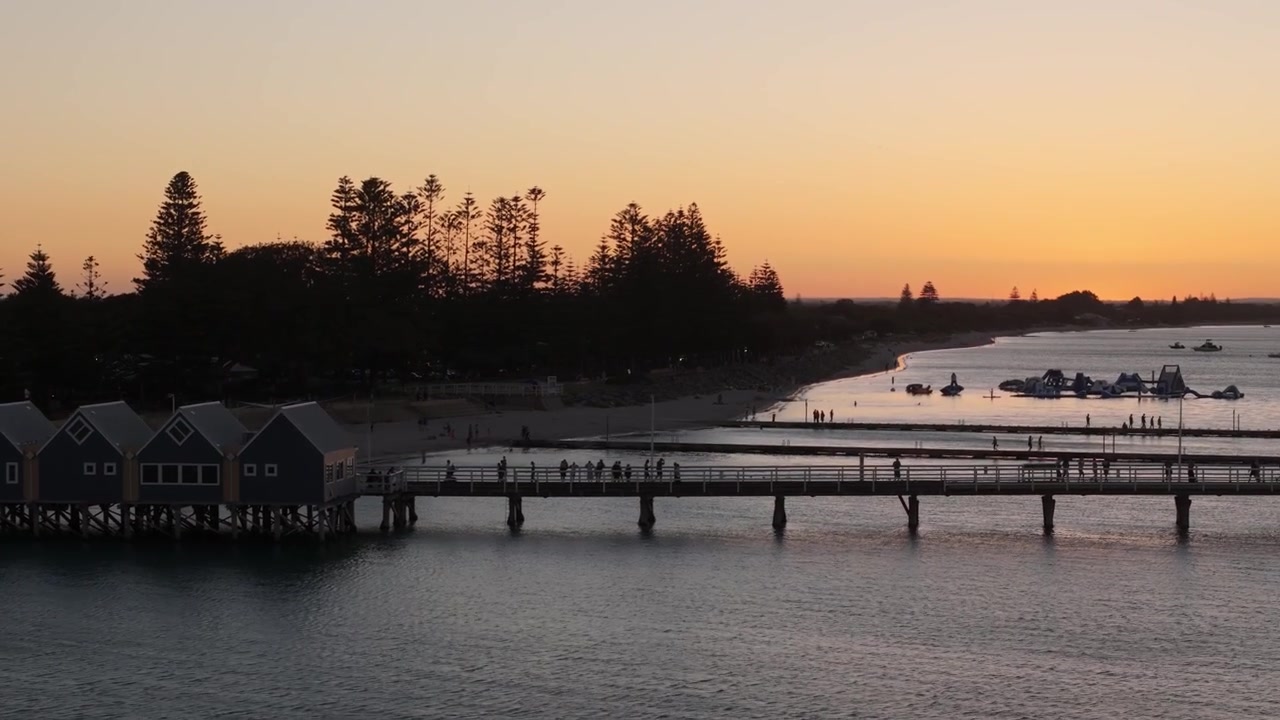 Aerial view of a bustling Busselton Jetty with a golden sunset in the background creating a soft glow in the air
