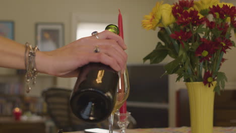 Frau-Gießt-Rotwein-In-Ein-Weinglas-In-Ihrem-Haus-Mit-Blumen-Und-Kerzen-Auf-Den-Tischen