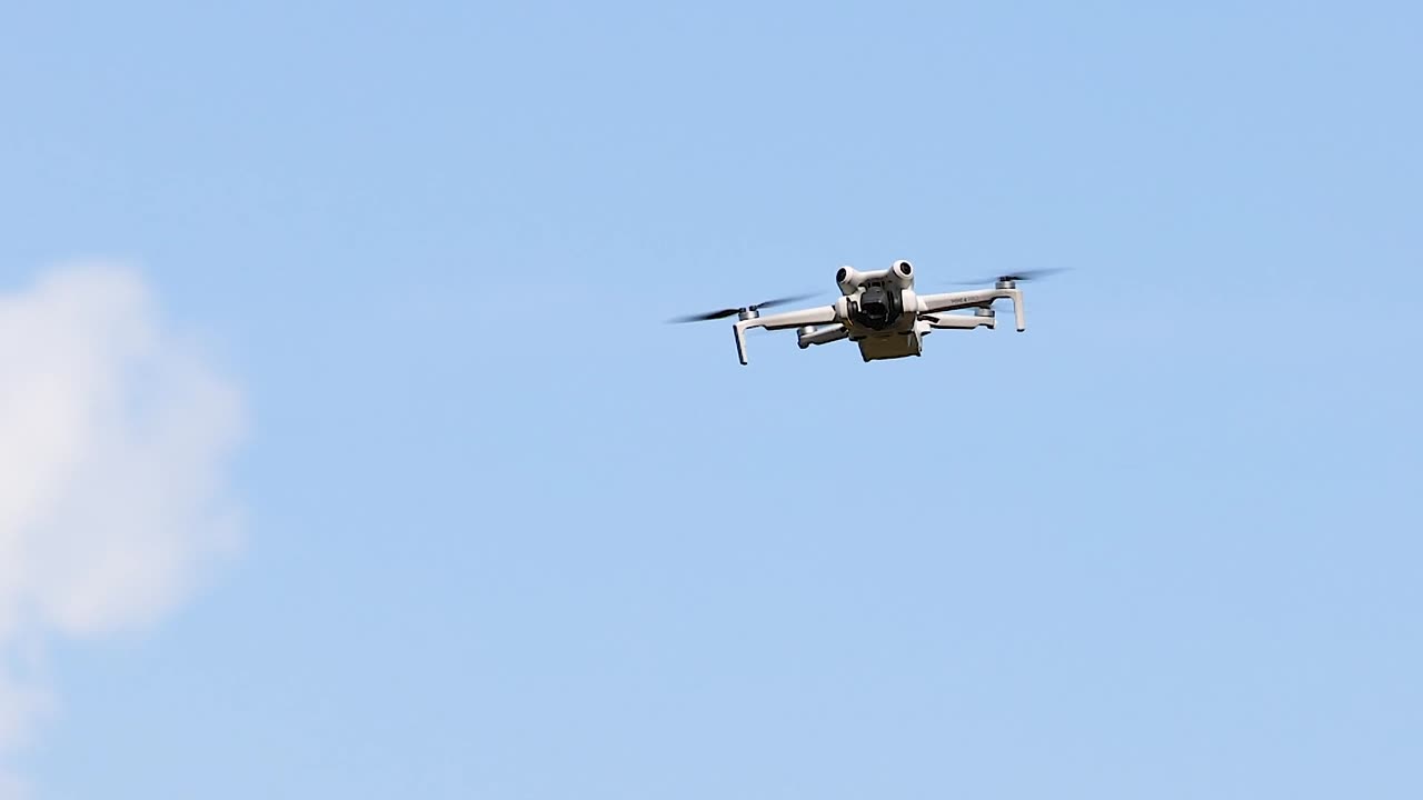 Un moderno drone telecomandato staziona stabilmente contro un cielo azzurro brillante con soffici nuvole.