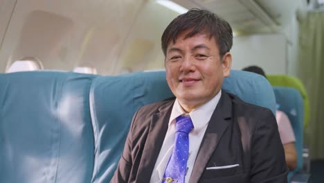 Portrait-of-Asian-executive-businessman-in-formalwear-looking-at-camera-with-smiling-face-in-business-class.-The-passenger-male-feeling-relax-and-happiness-to-travel-for-vacation-trip-on-airplane.