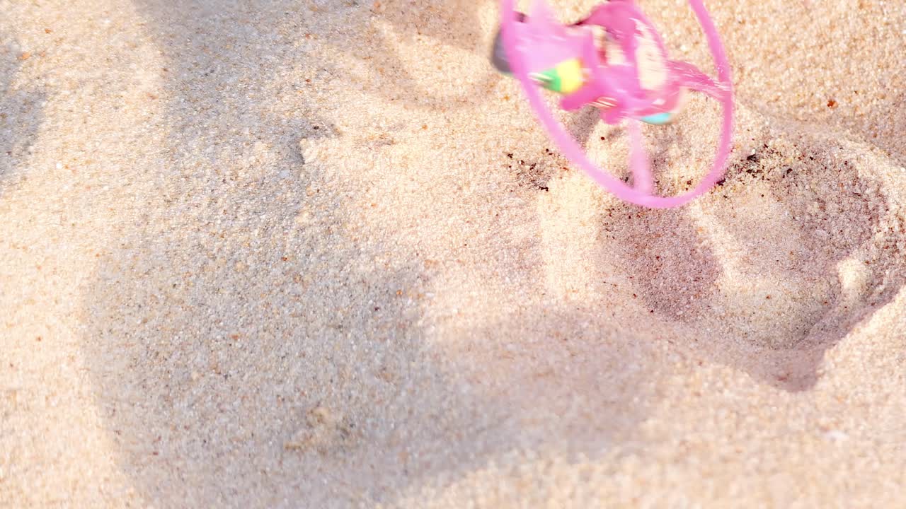 A vibrant toy spins and leaves patterns in the sand, creating playful impressions.