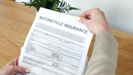 una mujer abriendo una carta de documento de seguro de motocicleta que describe su póliza y detalles de la cubierta