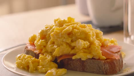 breakfast setting with freshly made scrambled eggs on smoked salmon with sourdough toast with coffee mug in background 4k.