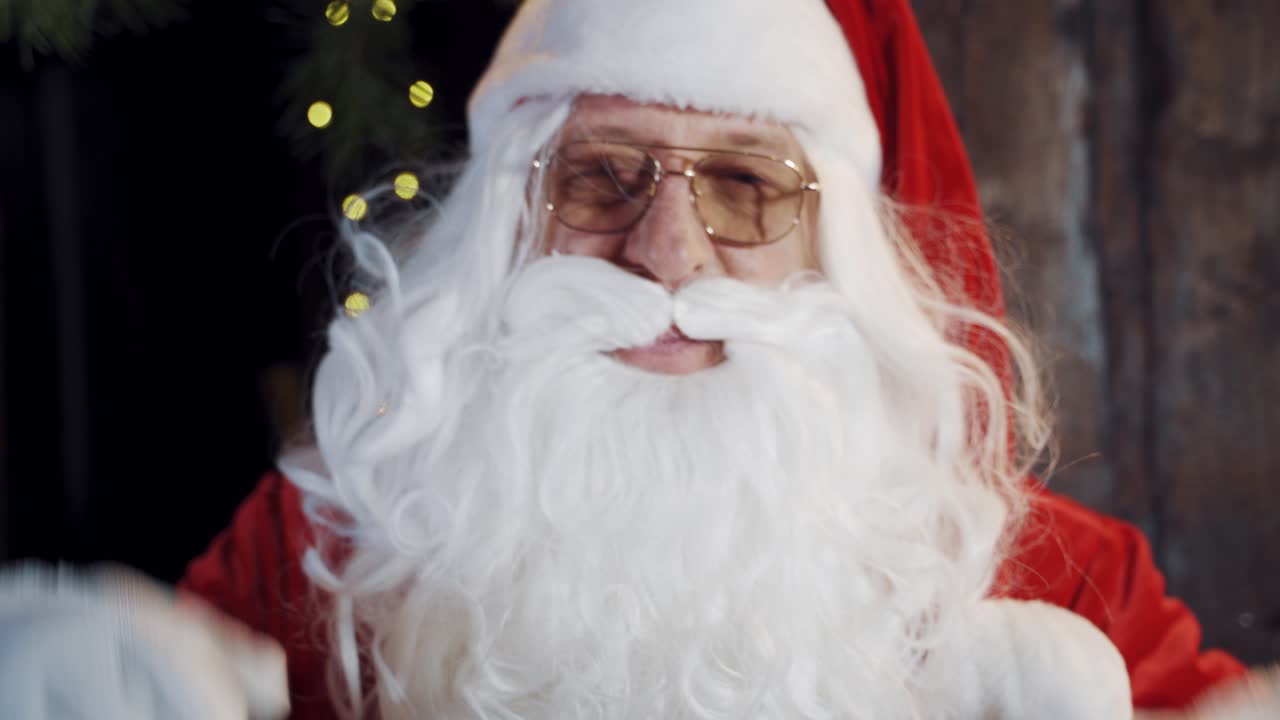 Close-up Santa with white beard wearing glasses. Portrait of Santa Claus in white and red costume in glasses inside the house.